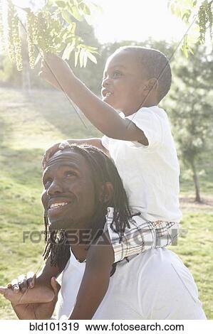 Stock Photo - African American man carrying son on shoulders. Fotosearch
