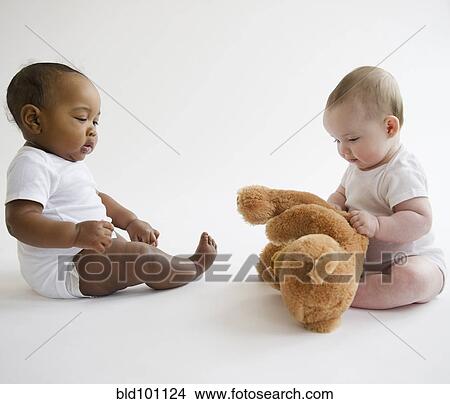 Picture - Babies sitting together on floor with teddy bear. Fotosearch