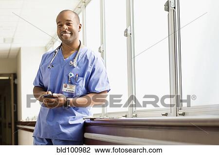 Stock Image - Black doctor using cell phone in hospital. Fotosearch