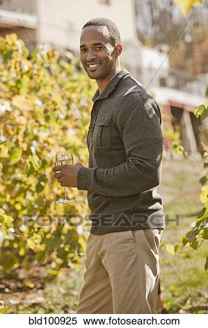Stock Photography - Black man drinking wine in vineyard. Fotosearch