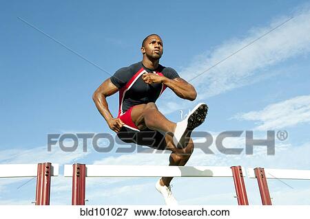 Stock Photo - Black runner jumping hurdles in track race. Fotosearch