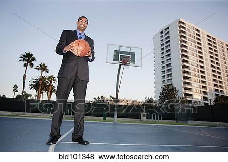 Stock Photo - Businessman holding basketball on basketball court. Fotosearch