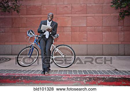 Businessman leaning on bicycle using digital tablet View Large Photo Image Stock Photo - Businessman leaning on bicycle using digital tablet. Fotosearch