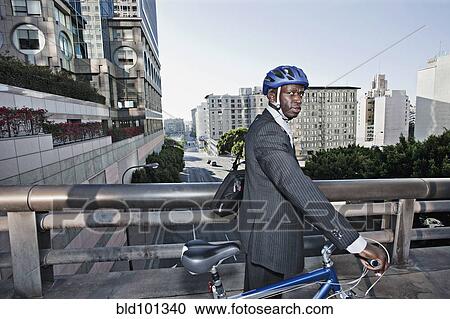 Stock Image - Businessman pushing bicycle over urban bridge. Fotosearch