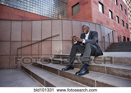 Stock Image - Businessman sitting on stairs text messaging on cell phone. Fotosearch