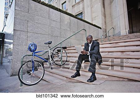 Businessman sitting on stairs using digital tablet View Large Photo Image Stock Image - Businessman sitting on stairs using digital tablet. Fotosearch