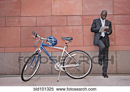 Stock Photography - Businessman using digital tablet near bicycle. Fotosearch