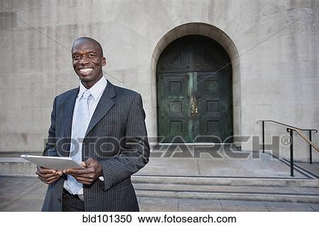 Stock Image - Businessman using digital tablet on urban sidewalk. Fotosearch