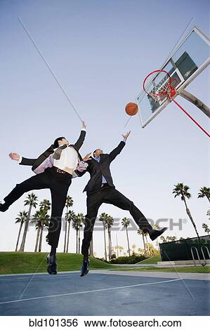 Stock Photograph - Businessmen playing basketball outdoors. Fotosearch