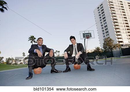 Picture - Businessmen sitting on basketballs on basketball court. Fotosearch