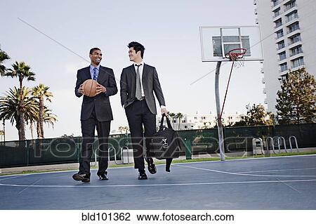 Stock Image - Businessmen walking on basketball court. Fotosearch
