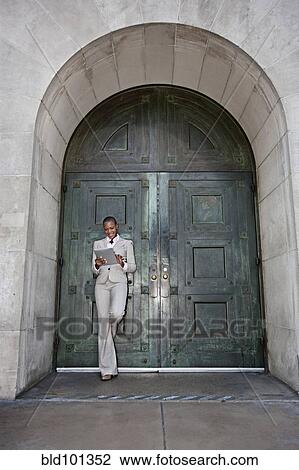 Stock Image - Businesswoman leaning against door using digital tablet. Fotosearch
