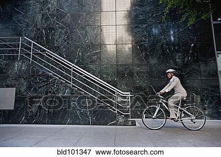 Stock Photo - Businesswoman riding bicycle on sidewalk. Fotosearch