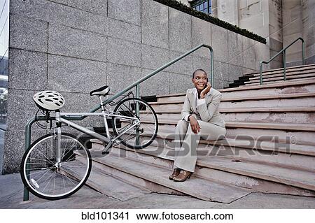 Stock Image - Businesswoman sitting in stairs talking on cell phone. Fotosearch