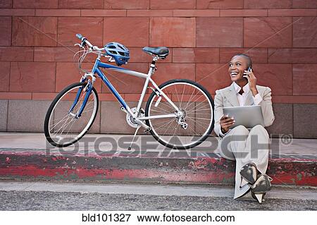 Stock Photo - Businesswoman sitting on curb using digital tablet and cell phone. Fotosearch