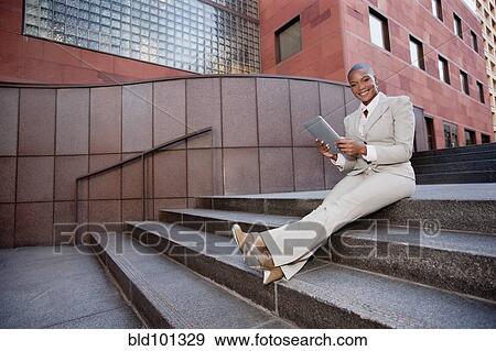 Stock Photo - Businesswoman sitting on stairs using digital tablet. Fotosearch
