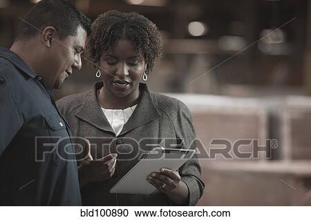 Stock Image - Businesswoman talking to worker in warehouse. Fotosearch