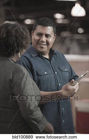 Stock Photo - Businesswoman talking to worker in warehouse. Fotosearch