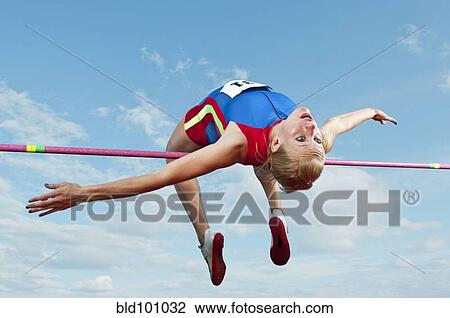 Stock Image - Caucasian athlete jumping over bar. Fotosearch