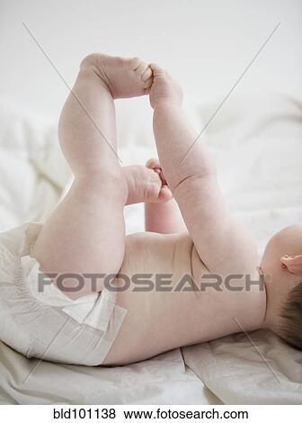 Stock Photo - Caucasian baby girl laying on blanket holding feet. Fotosearch
