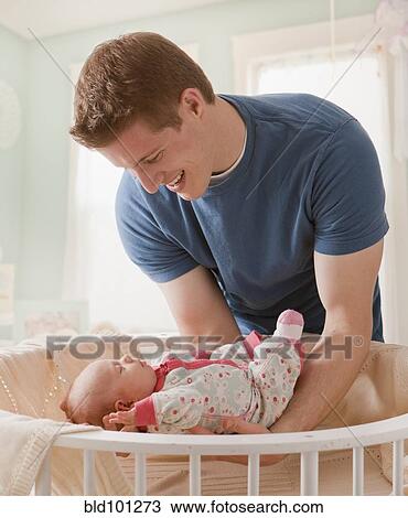 Stock Image - Caucasian father lifting baby girl from crib. Fotosearch
