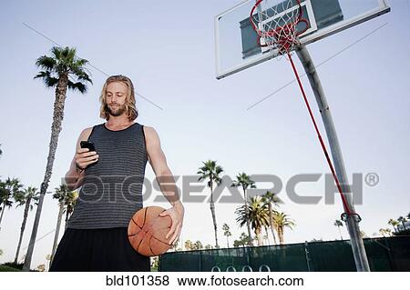 Caucasian man holding basketball and text messaging on cell phone View Large Photo Image Stock Photo - Caucasian man holding basketball and text messaging on cell phone. Fotosearch