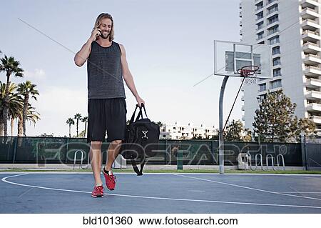 Stock Image - Caucasian man on basketball court talking on cell phone. Fotosearch