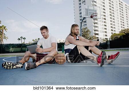 Caucasian men using cell phone and digital tablet on basketball court View Large Photo Image Picture - Caucasian men using cell phone and digital tablet on basketball court. Fotosearch