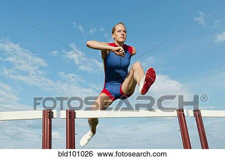 Stock Photograph - Caucasian runner jumping over hurdles on track. Fotosearch