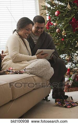 Couple looking at digital tablet on Christmas morning View Large Photo Image Stock Photo - Couple looking at digital tablet on Christmas morning. Fotosearch