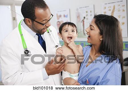 Stock Photo - Doctor and nurse standing with baby in doctor's office. Fotosearch