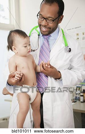 Stock Image - Doctor helping baby to walk in doctor's office. Fotosearch