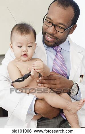 Doctor holding baby in doctor's office View Large Photo Image Stock Photograph - Doctor holding baby in doctor's office. Fotosearch