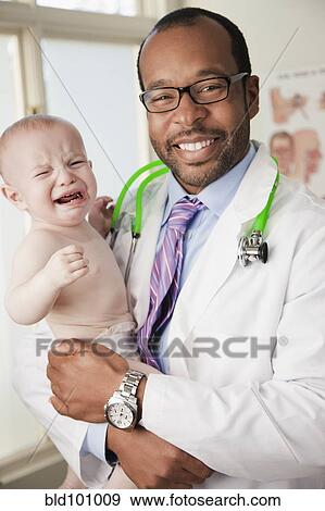 Stock Photo - Doctor holding crying baby in doctor's office. Fotosearch