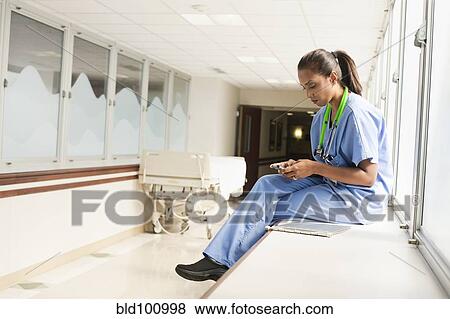 Stock Photo - Doctor text messaging on cell phone in hospital. Fotosearch