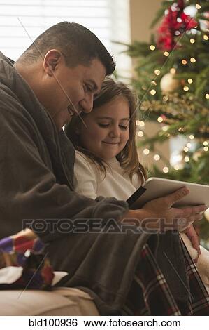 Stock Photograph - Father and daughter looking at digital tablet on Christmas morning. Fotosearch