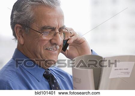 Stock Image - Hispanic businessman talking on cell phone and reading report. Fotosearch