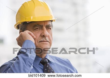 Stock Photo - Hispanic businessman wearing hard hat and talking on cell phone. Fotosearch