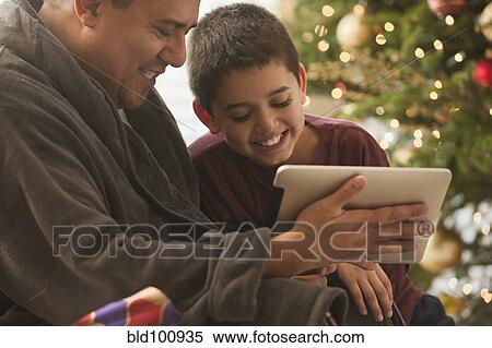 Stock Photography - Hispanic father and son looking at digital tablet on Christmas morning. Fotosearch
