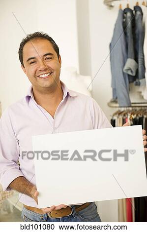 Stock Image - Hispanic man holding blank sign in clothing store. Fotosearch
