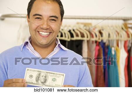 Stock Image - Hispanic man holding cash in clothing store. Fotosearch