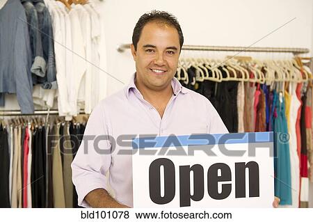Hispanic man holding open sign in clothing store View Large Photo Image Stock Photo - Hispanic man holding open sign in clothing store. Fotosearch