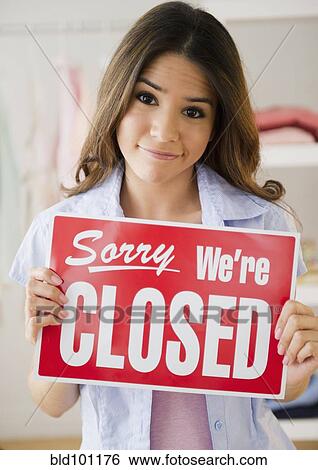 Stock Photograph - Hispanic woman holding closed sign in store. Fotosearch