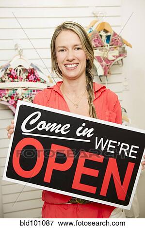Hispanic woman holding open sign in store View Large Photo Image Stock Photo - Hispanic woman holding open sign in store. Fotosearch