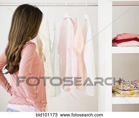Stock Image - Hispanic woman looking at clothing in closet. Fotosearch