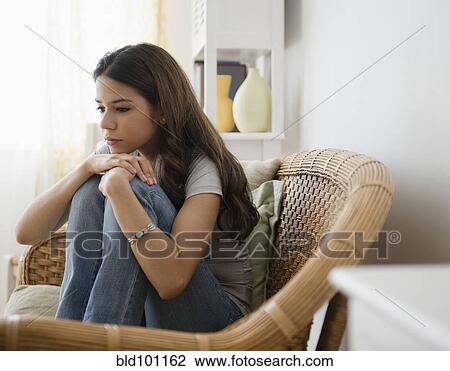 Stock Image - Hispanic woman sitting in chair thinking. Fotosearch