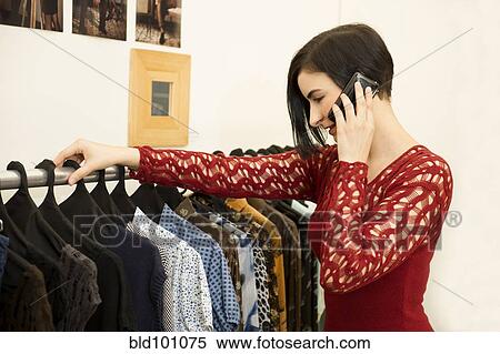 Stock Photography - Hispanic woman talking on cell phone in clothing store. Fotosearch