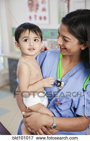 Stock Photo - Indian doctor holding baby in doctor's office. Fotosearch