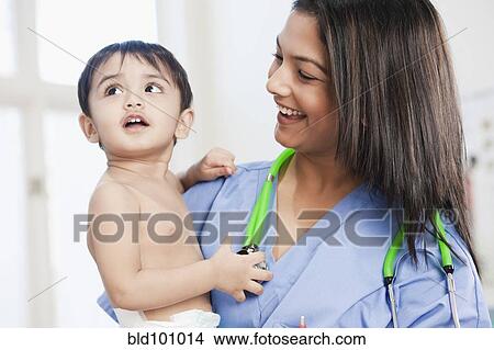 Picture - Indian nurse holding baby in doctor's office. Fotosearch