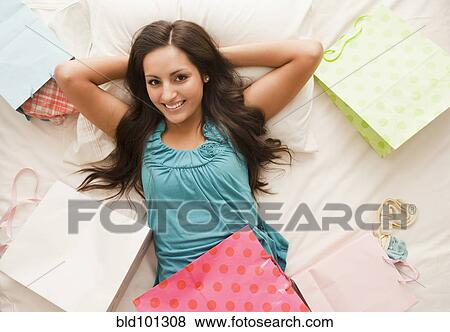 Stock Photo - Mixed race woman laying on bed with shopping bags. Fotosearch